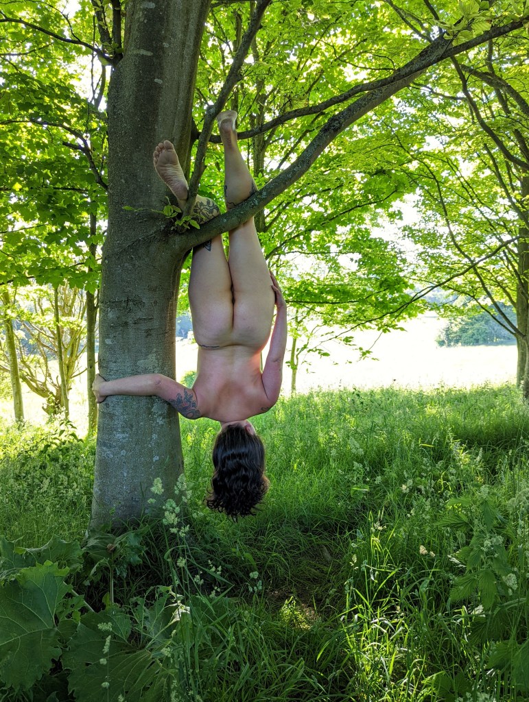 Kimi naked from behind hanging by her legs from a tree.