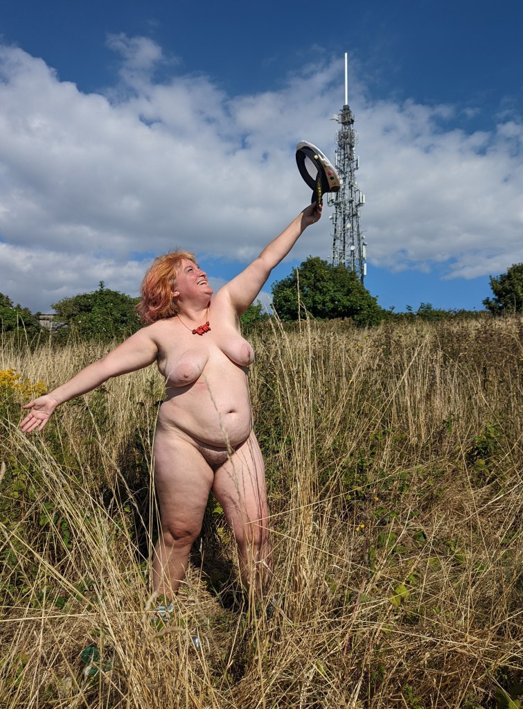 Dolly naked, left arm aloft holding captains hat.