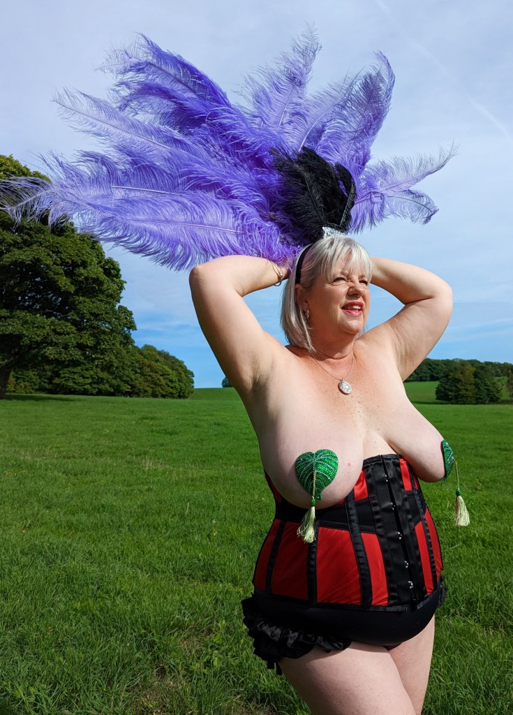 Lucy in Red corset with sparkling green leaf nipple tassels and blue feathers.