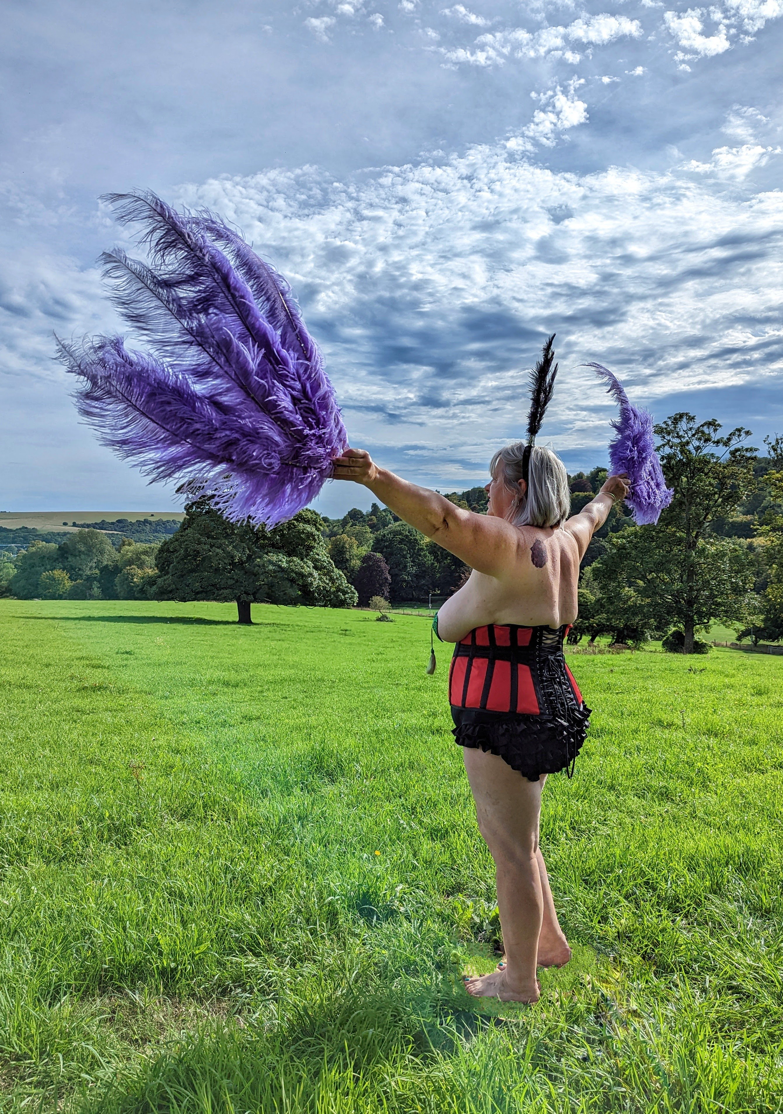 Lucy in Red corset with sparkling green leaf nipple tassels and blue feathers.