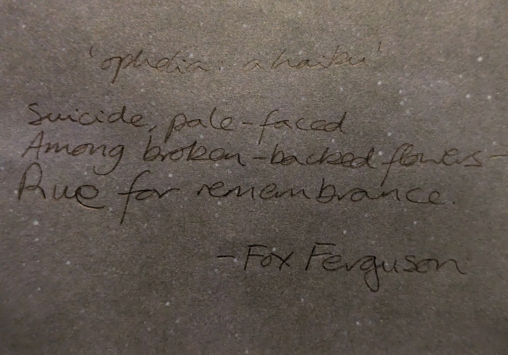 The haiku is a little hard to read in the photo and says - 

"Opelia a haiku -

Suicide, pale-faced
Among broken-backed flowers
Rue for remembrance" 
